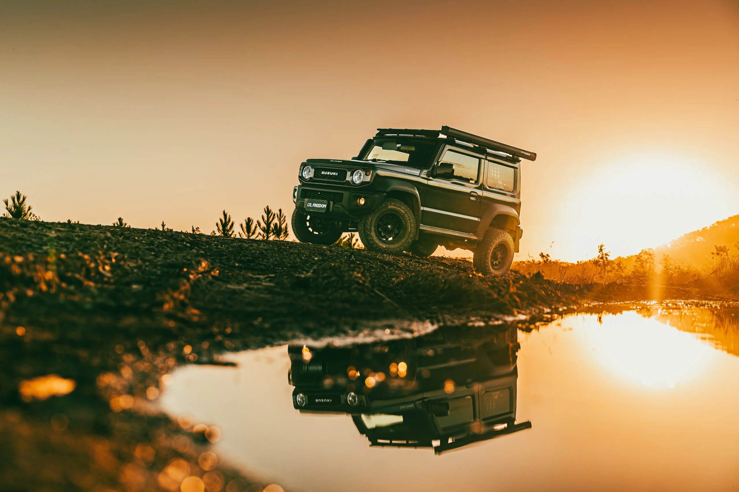 A four-wheel drive reflected in still water at sunset.